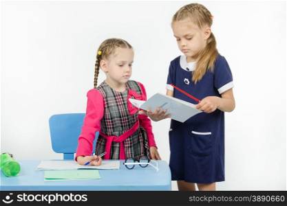 Two girls play school teacher and student. The teacher looks at pupils diary