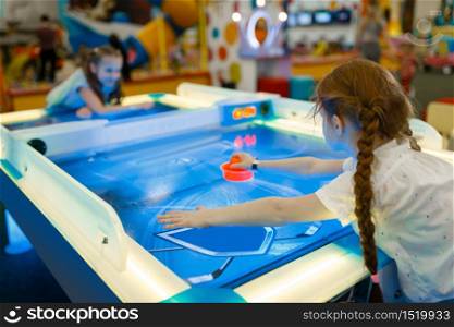 Two girls playing air hockey in the entertainment center. Children leisures on holidays, childhood happiness, happy kids on playground. Girls playing air hockey in entertainment center