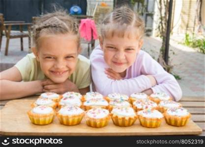 Two girls pretending funny faces, sitting in front of easter cupcakes