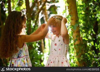 Two girls putting on tiaras in sunlit forest