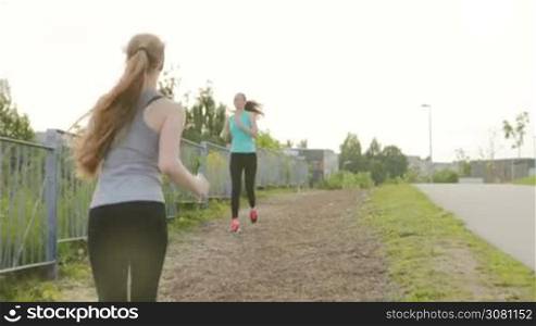 Two girls run along the walkway, meet and have fun talking in the park next to a lake at summer sunset