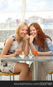 Two girls sit in cafe and smile, showing forward