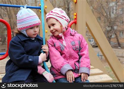 Two girls sit on playground, happy and sad