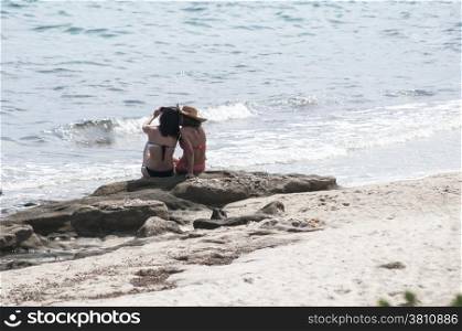 Two girls sitting back on sea beach rock