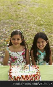 Two girls sitting in front of a birthday cake
