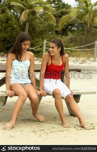 Two girls sitting on a bench at the beach