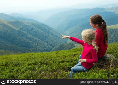 two girls sitting on a grass and looking at the mountains