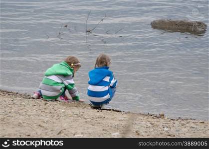 Two girls sitting on a river bank. Two children enthusiastically walk along the river bank