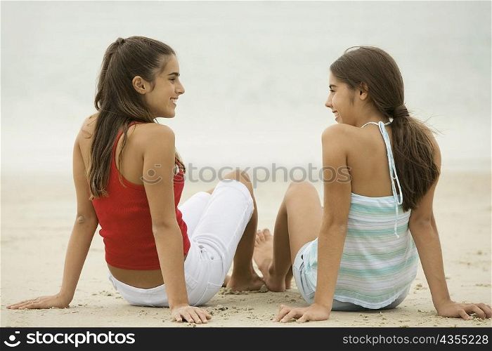 Two girls sitting on the beach laughing