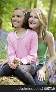 Two girls sitting together in a wood full of bluebells