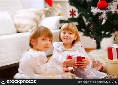 Two girls sitting with presents near Christmas tree&#xA;