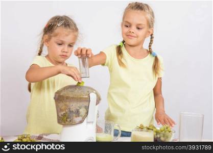 Two girls squeezed juice in a juicer. Two girls at a table squeezed juice from pears and grapes with a juicer