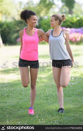 two girls stretching leg muscles outdoors in a park
