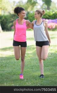 two girls stretching leg muscles outdoors in a park