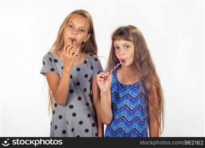 Two girls suck lollipops and look in the frame