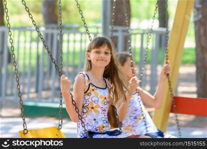 Two girls swing on a swing in a city park