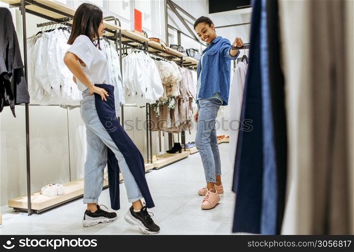 Two girls trying on clothes in clothing store. Women shopping in fashion boutique, shopaholics, shoppers looking garment on hangers. Two girls trying on clothes in clothing store