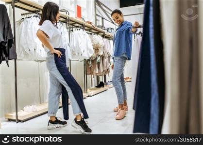 Two girls trying on clothes in clothing store. Women shopping in fashion boutique, shopaholics, shoppers looking garment on hangers. Two girls trying on clothes in clothing store