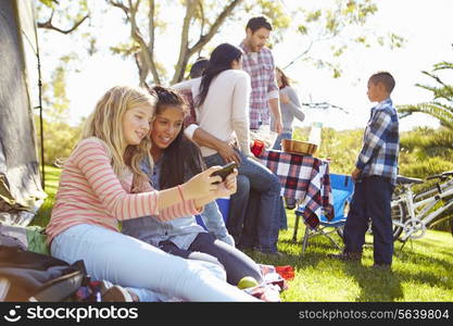 Two Girls Using Mobile Phone On Family Camping Holiday