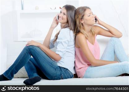 two girls with smartphones sitting on sofa at home