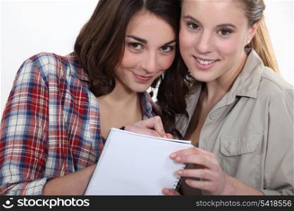 Two girls writing on a notebook