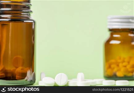 Two glass bottles of drugs. Scattered white round tablets next to each other. Green flat background.. Two glass bottles of pills. Scattered white round tablets next to each other. Green flat background.