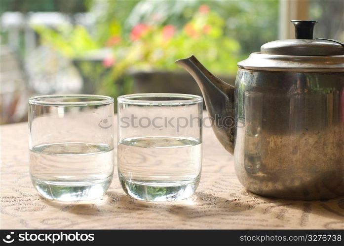 Two glass cups and steel teapot on the table near window