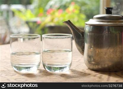 Two glass cups and steel teapot on the table near window