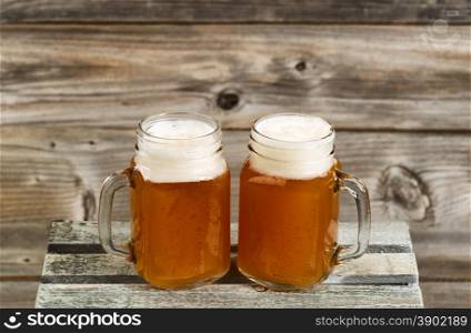 Two glass jars filled with frosty cold beer on top of wooden crate with rustic wood in background.