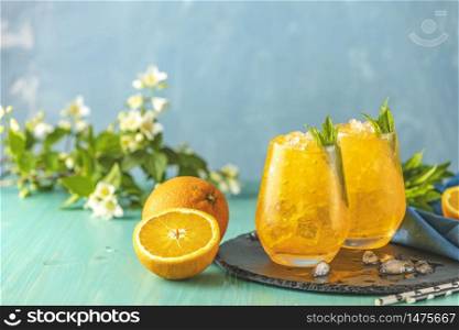 Two glass of orange ice drink with fresh mint on wooden turquoise table surface. Fresh cocktail drinks with ice fruit and herb decoration. Alcoholic non-alcoholic drink-beverage.