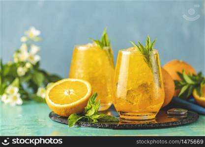Two glass of orange ice drink with fresh mint on wooden turquoise table surface. Fresh cocktail drinks with ice fruit and herb decoration. Alcoholic non-alcoholic beverage. Mojito on blue background