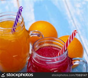 Two glass vessel with the juice of orange and grapefruit with a straw on a blue table