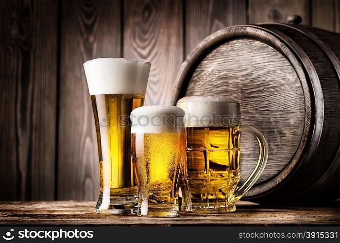 Two glasses and mug of light beer on a background of the old wooden barrels. Two glasses and mug of light beer