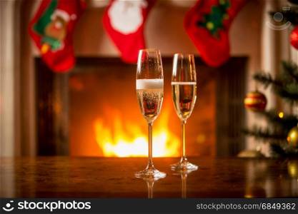 Two glasses being filled with champagne on Christmas table in front of fireplace