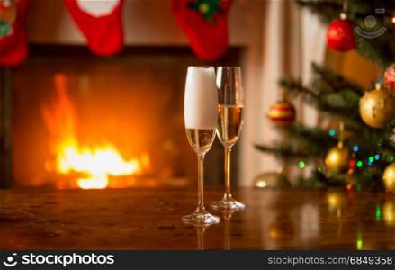 Two glasses being filled with champagne on table next to Christmas tree