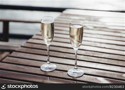 Two glasses filled with ch&agne on wooden table outdoors. . Two glasses of ch&agne on table