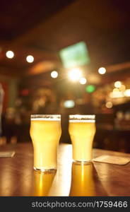 Two glasses full of fresh foamy beer on wooden counter in bar, nobody. Pub theme concept, night lifestyle, nightstyle symbol, restaurant interior on background. Two glasses full of fresh foamy beer on counter