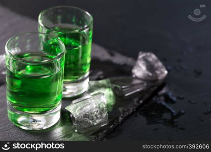 Two glasses of absinthe and melted ice cubes on a black background. Two glasses of absinthe and melted ice cubes