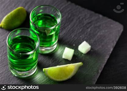 Two glasses of absinthe with lime slices and pieces of sugar on a dark background. Two glasses of absinthe with lime slices and pieces of sugar