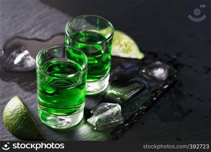 Two glasses of absinthe with melted ice and slices of lime and on a black background. Two glasses of absinthe with melted ice and slices of lime