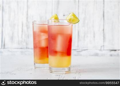Two glasses of Bay Breeze cocktail garnished with lime wedges on wooden background