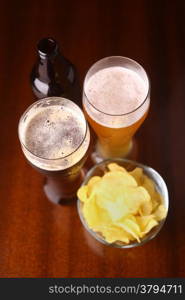 Two glasses of beer and potato chips on a wooden table