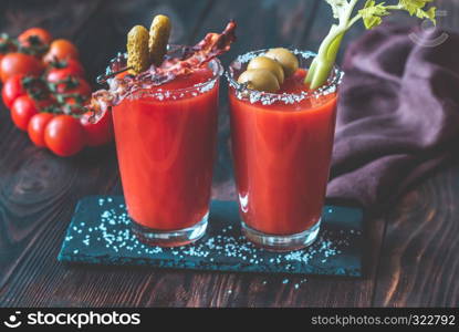 Two glasses of Bloody Mary garnished with gherkins, fried bacon strips, green olives and celery stalk