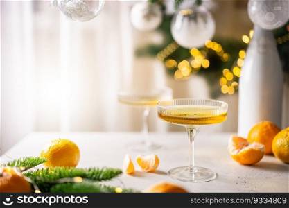 Two glasses of ch&agne and tangerines on a table against blurred christmas background with christmas lights. New year celebration party. Two glasses of ch&agne