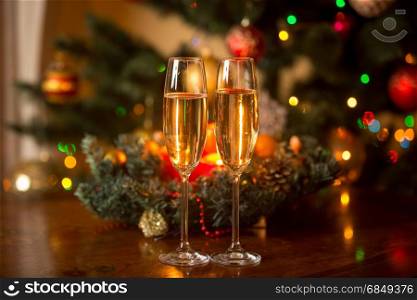 Two glasses of champagne and Christmas wreath with candles on wooden table