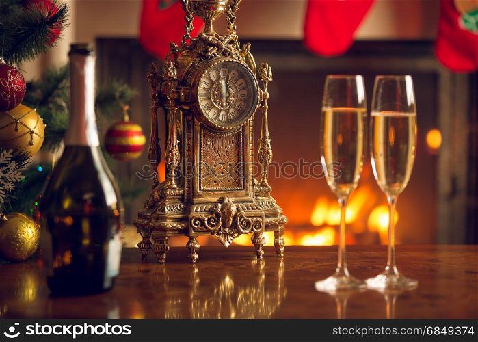Two glasses of champagne on table next to old clock show 12 o&rsquo;clock.