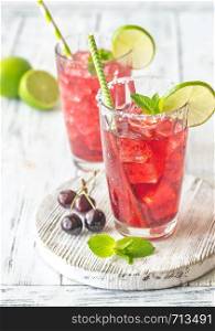 Two glasses of cherry mojito garnished with lime slices