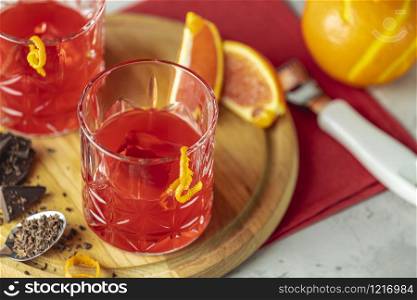 Two glasses of chocolate red orange negroni, an italian cocktail, an aperitif, first mixed in Firenze, Italy, in 1919, alcoholic bitter cocktail served by ingredients on the light gray table.