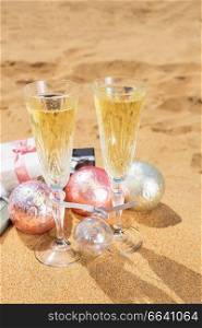 Two glasses of christmas ch&agne and bubbles with christmas gifts and decorations on beach. Two glasses of christmas ch&agne