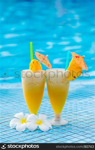 two glasses of cocktail beautifully decorated with pineapple and flowers on the edge of the pool
